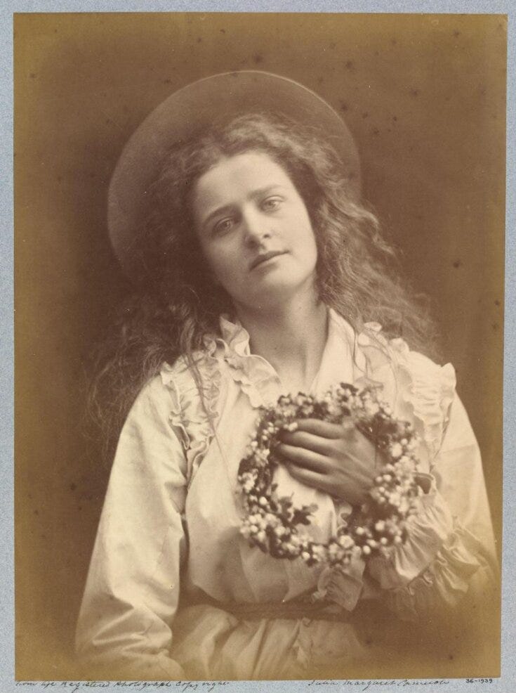 An antiquated wet-plate photograph of a young girl with long flowing hair, a wide-brimmed hat and a pleated white dress holding a wreath of flowers to her chest.