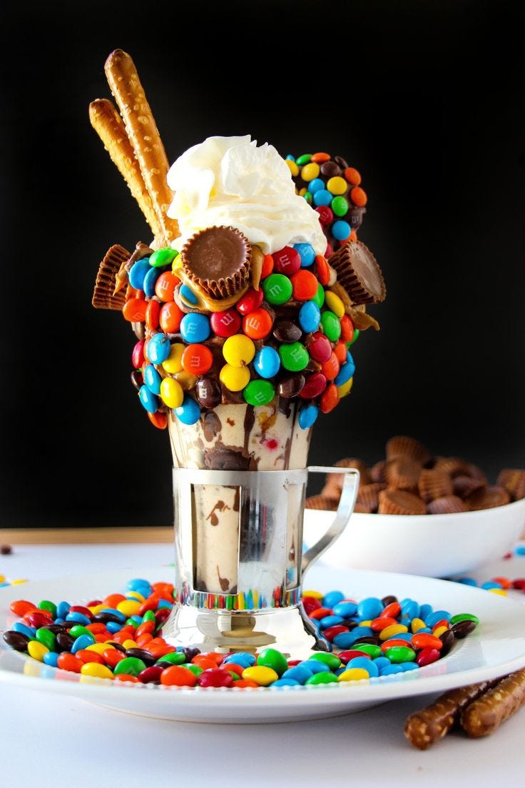 A colourful milkshake full of M&Ms and chocolates along with whipped cream and thick chocolate ice cream.