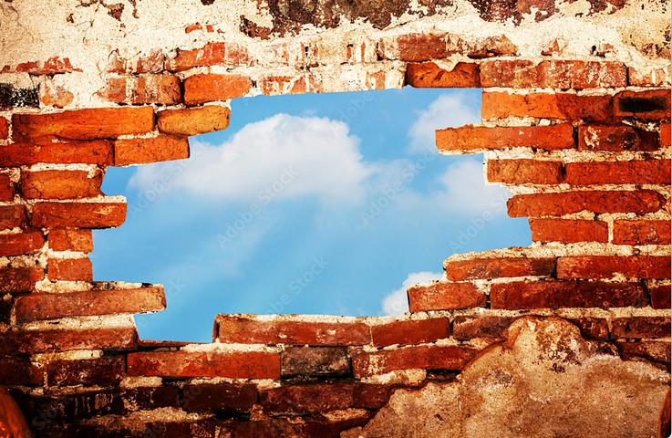 Red brick wall with a hole in the middle. The blue sky with clouds is visible through the hole.