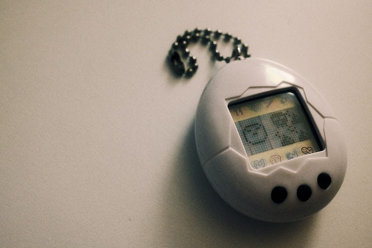A grayish Tamagotchi lays on a white backdrop, begging to be cared for my its oblivious owner.
