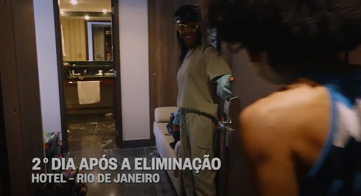 Conka abrindo a porta do hotel para receber a entrevistadora enquanto traja roupa monocromática