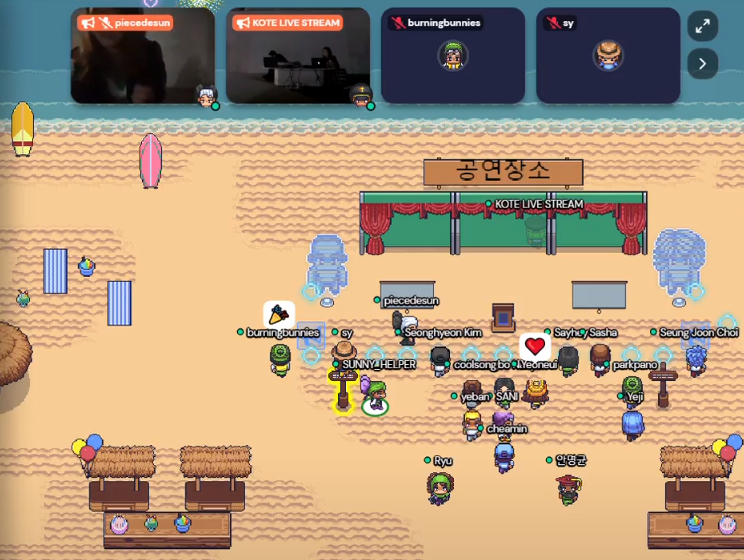 An image of the virtual space within Gather Town, which shows avatars assembled in front of a stage. There are four “screens” showing the different audio visual performances.