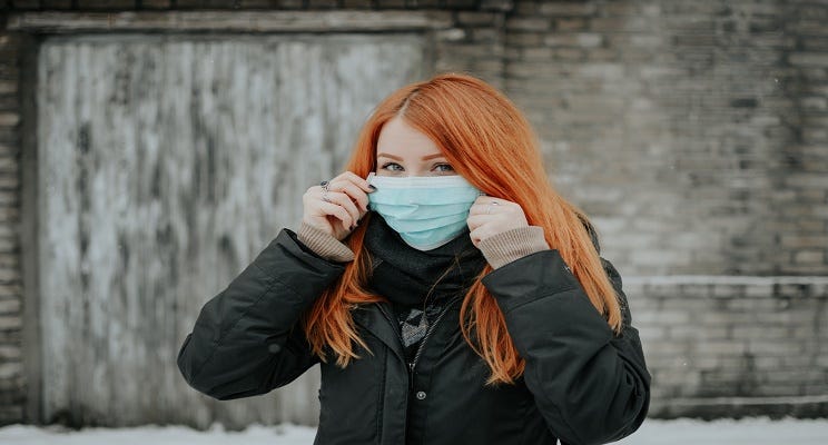 A red-haired woman wearing a disposable face mask.