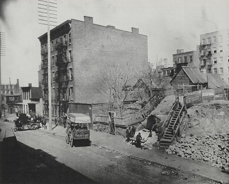 A brick tenement building next to a wooden shack and rubble.