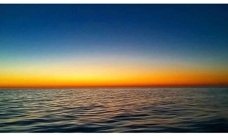 a vivid electric-orange sunset over the dark blue ocean at dusk in baja mexico