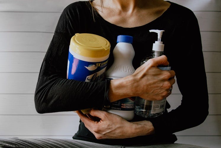 A woman holding 3 cleaning products in her arms