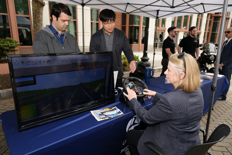 FMCSA Acting Deputy Administrator Sue Lawson (seated) tries Morgan State University’s driving simulator as two students (left) explain how it works.
