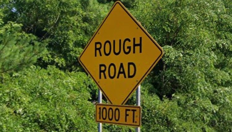 A yellow road sign reading “rough road 1000 ft”