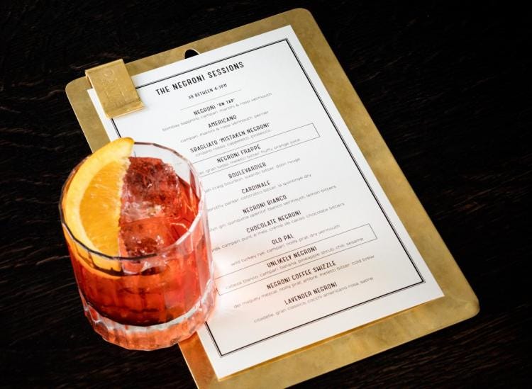 A Negroni Cocktail with an Orange Wedge sits atop a Negroni Sessions Menu on a Brass Clipboard