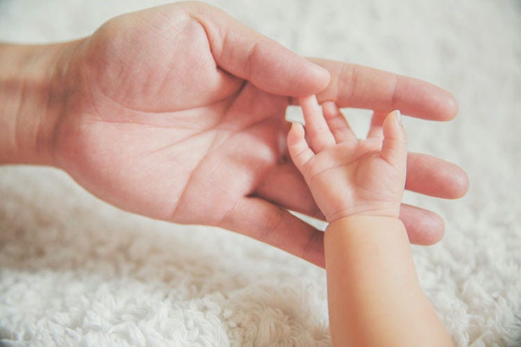 Adult hand holding a baby’s hand.