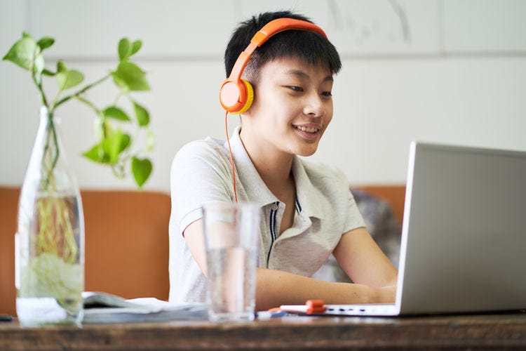 Boy at a table with headphones on, looking at a computer, smiling.