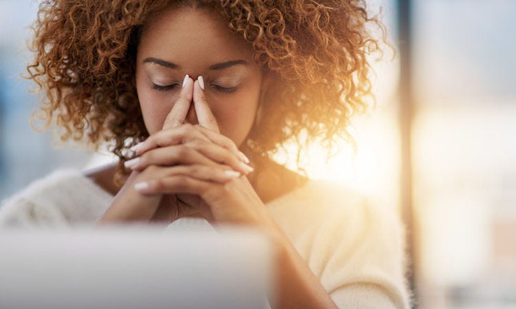 Woman with her hands folded, leaning her face into her hands, seeming stressed or contemplative.