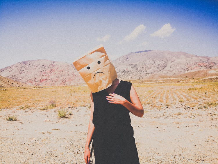 woman with sad paper bag on her head in an arrid area