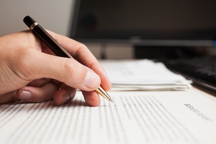 Hand poised to write or edit the text on several pieces of paper in a pile on a surface.