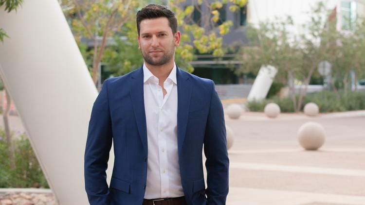 Jeff Kunowski poses in a white dress shirt and blue suit jacket in front the SkySong building in Scottsdale, AZ.