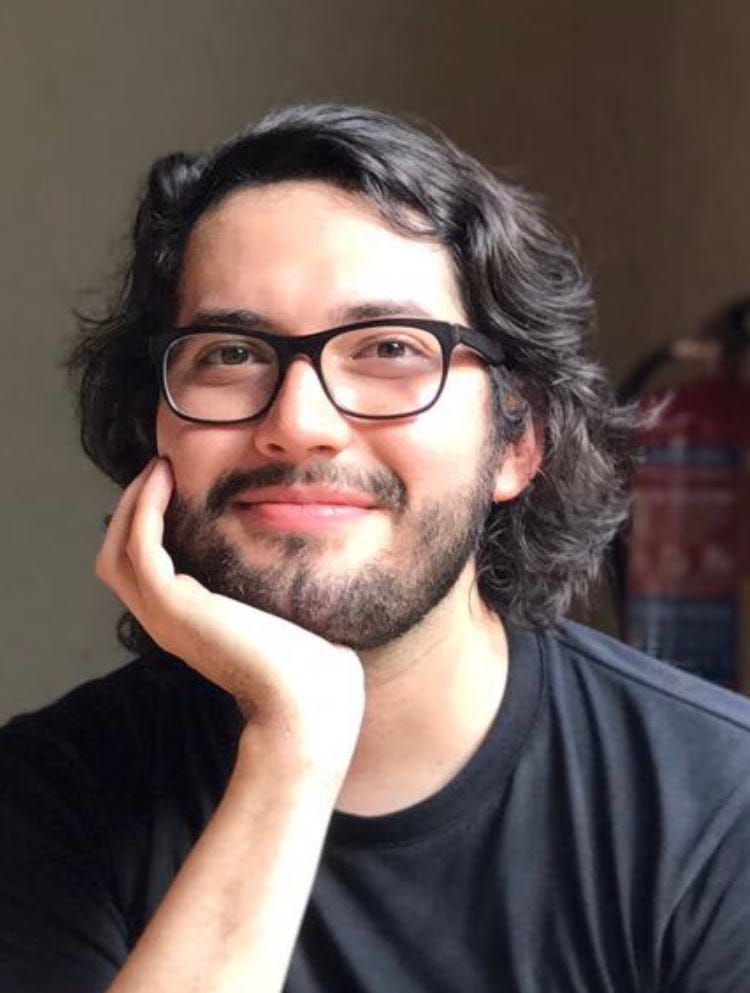 A person with long hair and beard and wearing glasses looks at the camera.