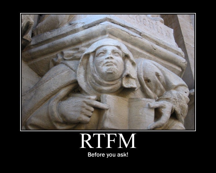 A sculpture on on a building showing a person holding a book and pointing to it with their index finger. The caption underneath reads “RTFM before you ask!”.