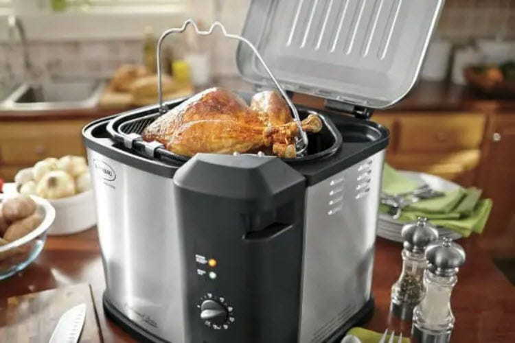 A stainless steel deep fryer on a kitchen counter, with a whole fried chicken in the basket.