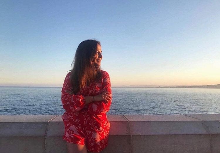 A female traveler poses for a picture on the coast of a beach at sunset