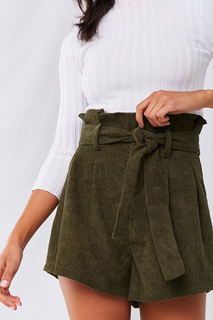 A Forever 21 model wearing olive green paper bag corduroy shorts with a ribbed white long sleeve top.