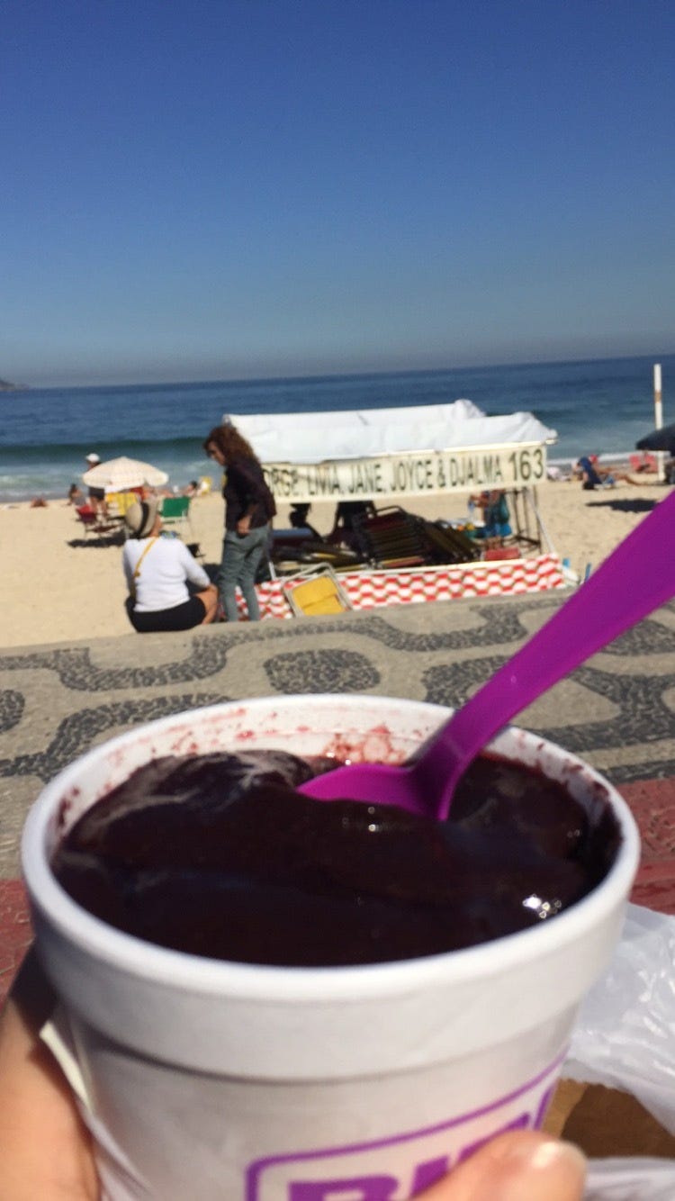 A view of the ocean and a beach and a cup of purple dessert with a spoon in it.