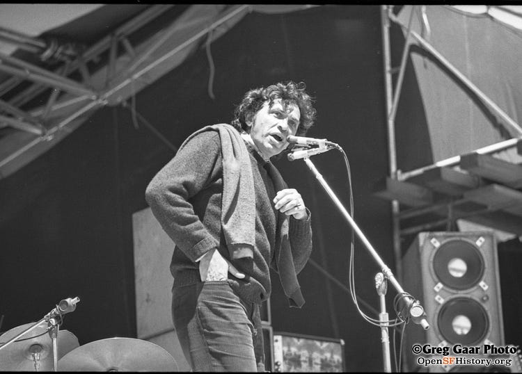 Black and white photo of Bill Graham talking into a microphone onstage at Kezar.