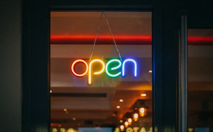 An ‘open’ sign on a shop window in rainbow colours