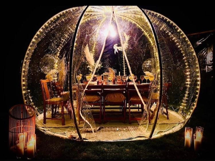 Image of an outdoor party pod/dining dome at night, lit up with fairy lights
