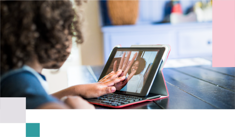a young girl sitting in front of a laptop, on Facetime with Mom, both touching the screen as if holding hands