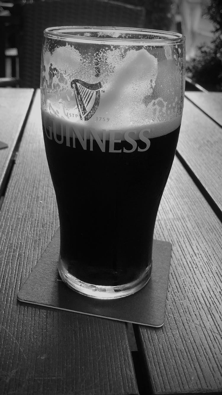 A black and white photo of a pint of Guinness half-drunk, on a table with a beer mat.