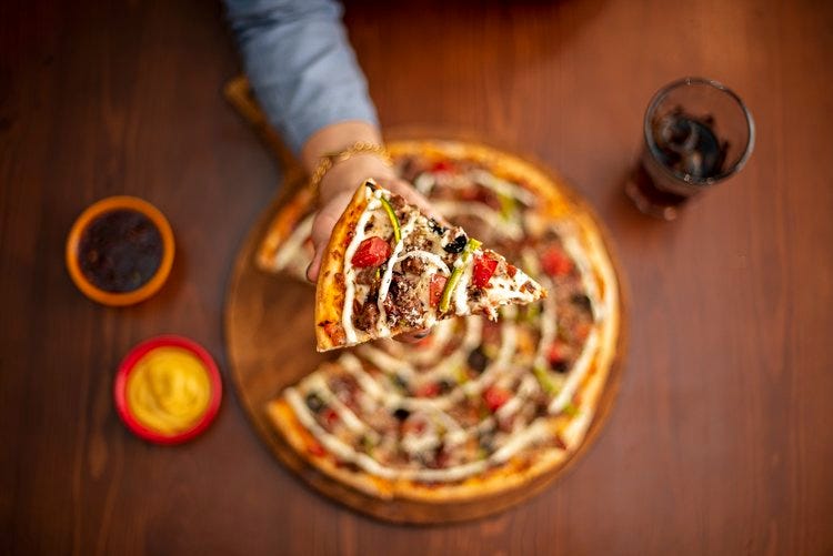 Someone is holding a slice of pizza with many unique toppings over a table.