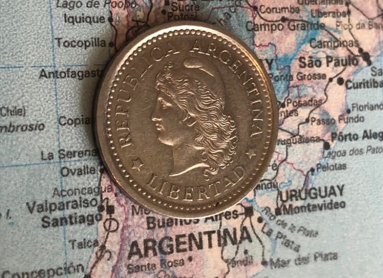 An Argentianian coin with the text “Liberty” on top of a map of Argentina