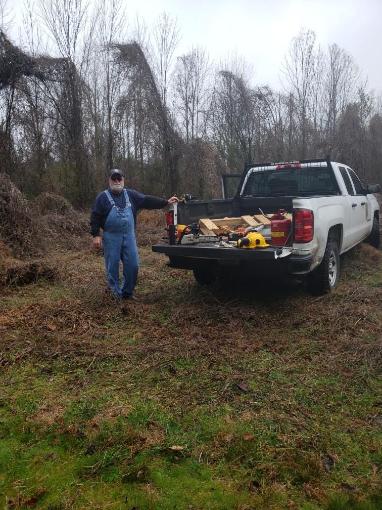 John stands next to the tailgate of a refuge pickup truck parked in a recently cleared patch of land