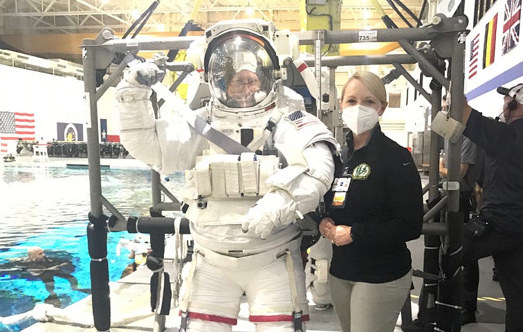 Danielle Anderson stands beside an astronaut in a space suit engaging in physical therapy exercises in a pool facility.