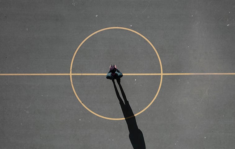 Aerial photo of a man standing in the center of a big painted circle and line running through the middle of it.