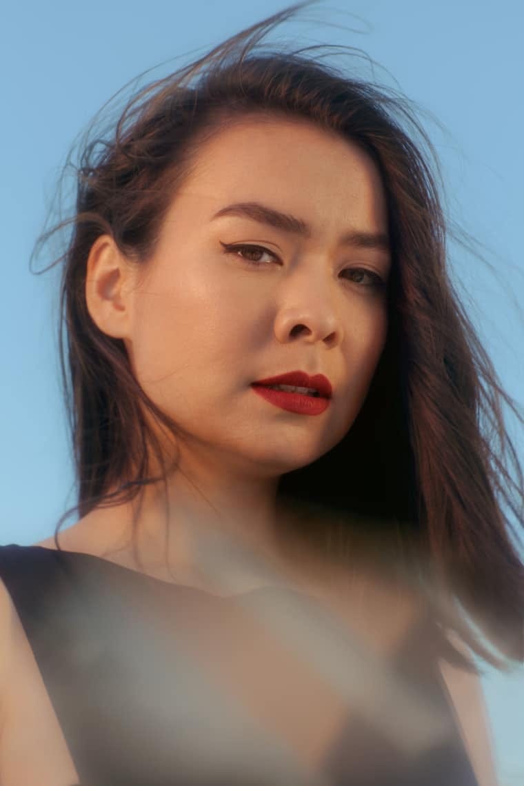 Portrait of a half East Asian, half white woman with long, straight dark hair and light skin. She wears read lipstick and a black blouse.