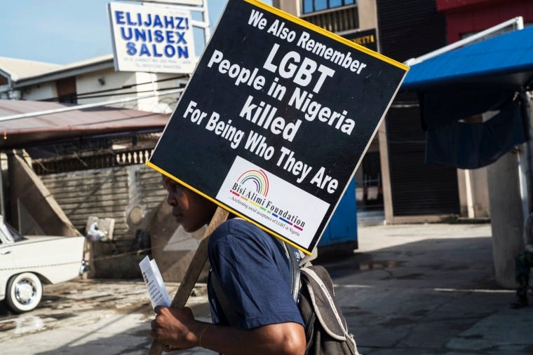 Protester carries sign: We also remember LGBT people in Nigeria killed for being who they are. In the background, there’s a business sign marking Elijanzi Unisex Salon.