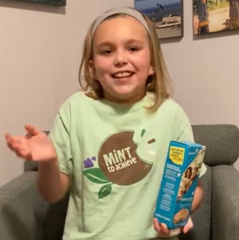 Young blonde girl holding box of Girl Scout cookies and gesturing