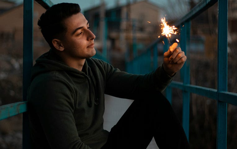 A sad young man holding a lit firework in his hand