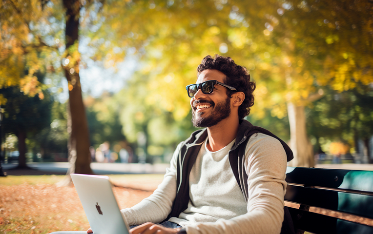 A man sitting on a park bench in a beautiful park with a laptop on his lap. Smiling, and enjoying himself because he has extra free time after installing a Chrome Extension that helps him engage with his community more effectively.