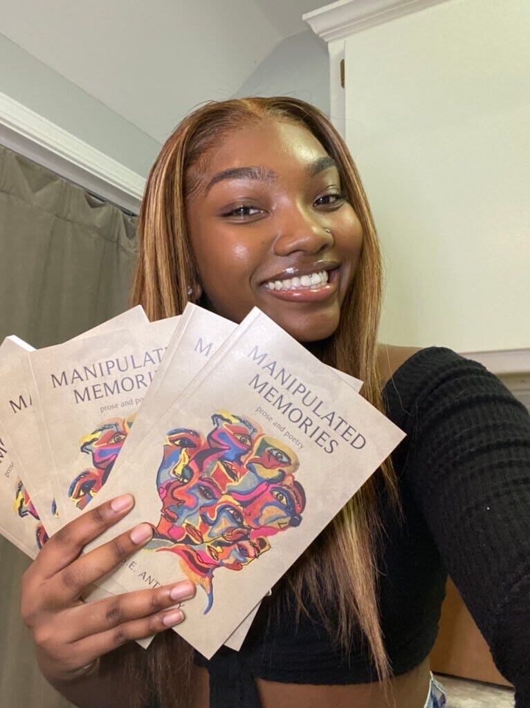 A young woman author smiles as she holds up copies her poetic memoir, titled Manipulated Memories.