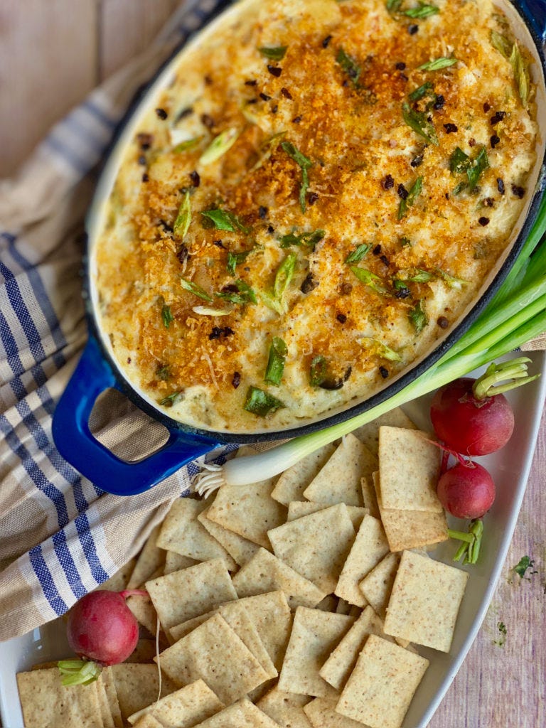bowl of bubbly artichoke dip surrounded by crackers green onion and turnips