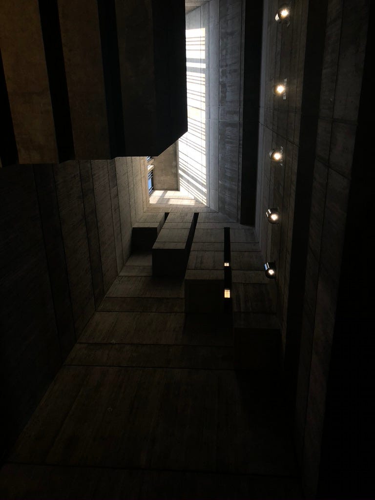 A dark ceiling made of concrete in Boston City Hall. On the top left, light pours through a tall window and casts long lines of white onto the ceiling.