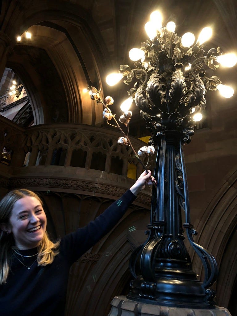 A woman holding up a budded cotton plant next to wrought iron decorative lights