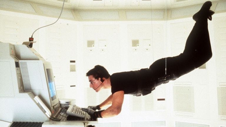 Captivating still from the 1996 Paramount Pictures’ Mission Impossible film, featuring Ethan Hunt (Tom Cruise) suspended on a wire, conducting a high-stakes operation on a state-of-the-art computer within a secure, hermetically sealed facility.