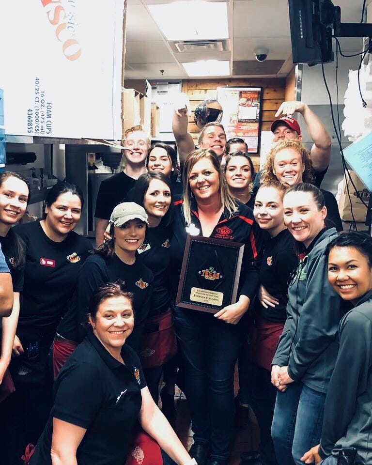 A groups of people smile at the camera, while the woman in the middle holds a plaque.