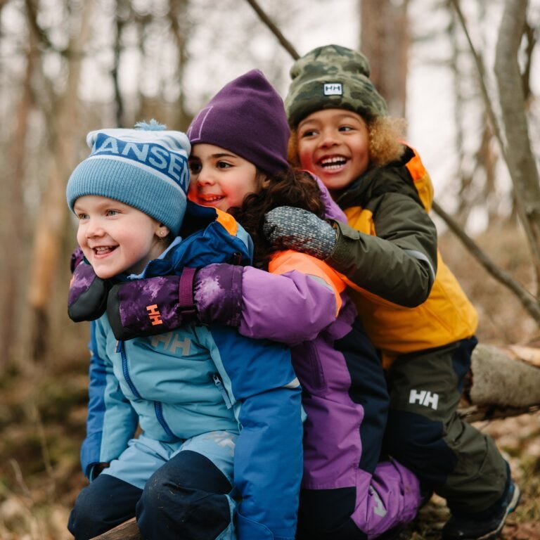 Three kids playing in the on a mountain in the cold wearing Helly Hansen ski jackets, ski pants, and beanies.