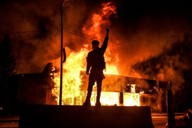 A protester raises a clenched fist in front of a burning building in Minneapolis. (AFP Photo)