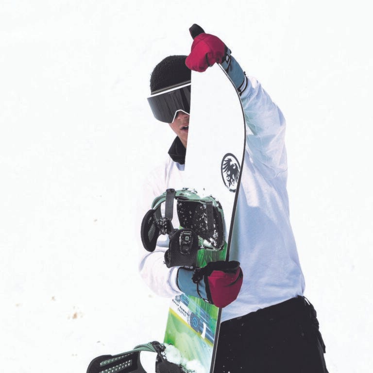 Male holding a never summer snowboard on top of the mountain.