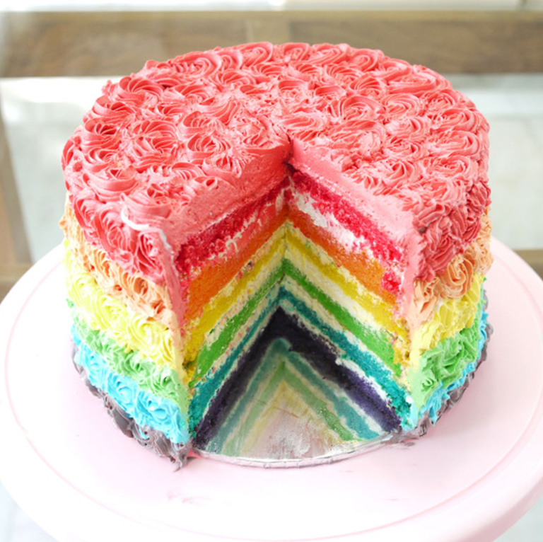Cake made up of rainbow layers, with one slice cut out from it.